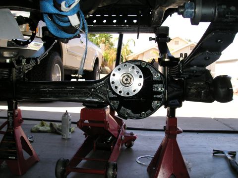 1986 Toyota Hilux - Rear view from under a truck of a freshly painted black solid front axle housing being fitted, third-member flange bolted up with the pinio…