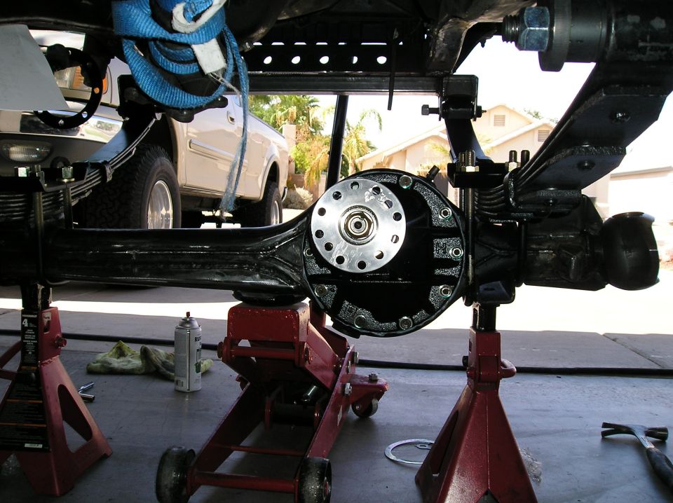 Black-painted solid front axle housing on floor jack under a truck during a straight-axle swap