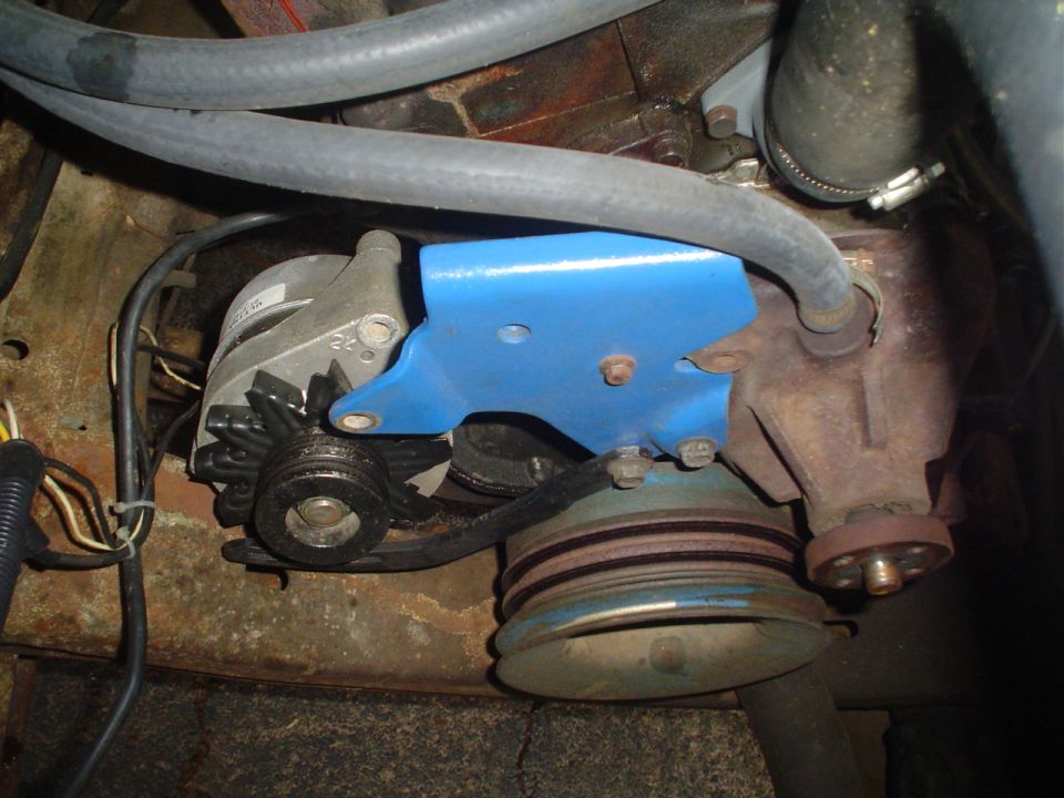 Close-up of an alternator mounted with a blue bracket, connected to engine pulleys and belts