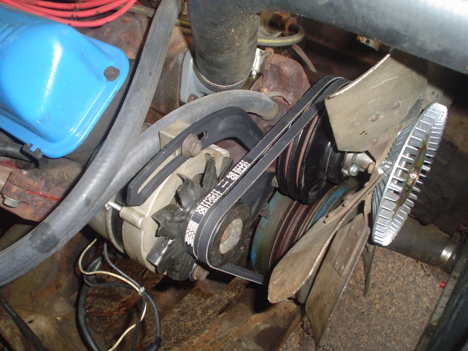Close-up of engine belts, alternator, and fan blades. Belt has text printed on it