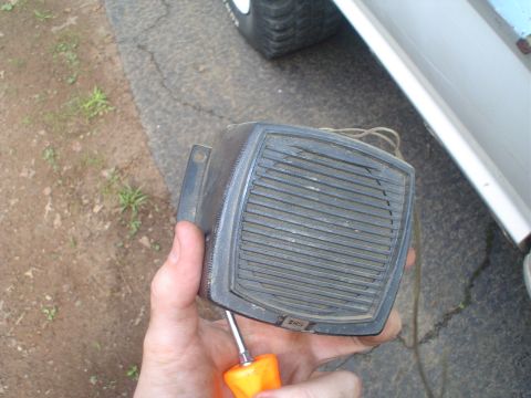 1967 Ford F-250 - A hand holds a black speaker part with a horizontal grille, with a screwdriver tip visible.