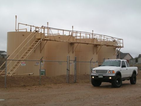 1996 Ford Bronco - White Ford Ranger pickup truck parked in front of large industrial storage tanks.