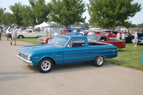 1967 Ford Ranchero - A blue pickup truck is parked at an outdoor car show with other vehicles and tents visible.