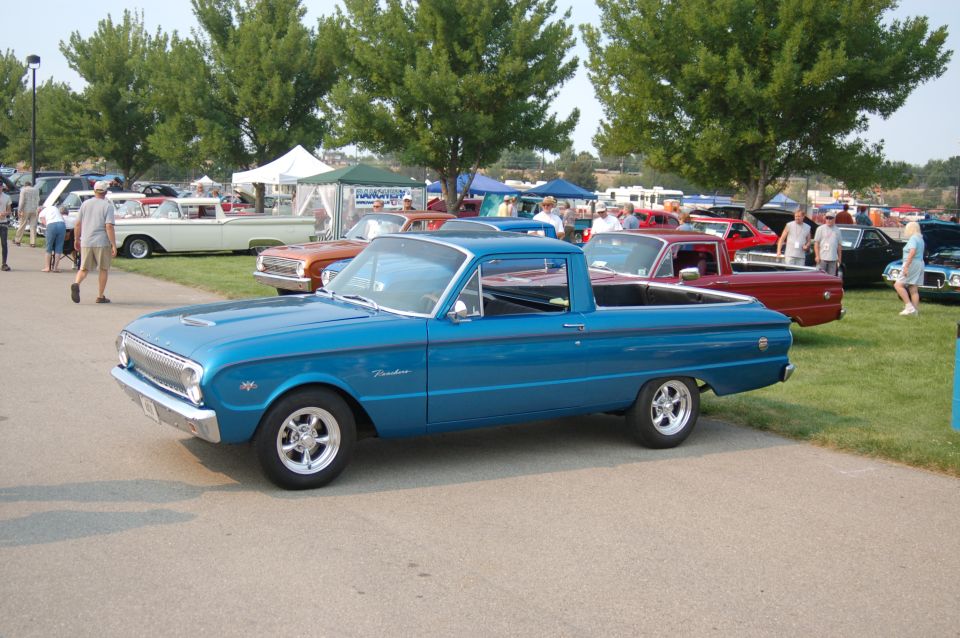 Blue pickup truck with 'Ranchero' script on fender. Other cars and tents in background