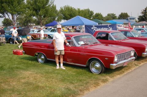 1967 Ford Ranchero - A man poses with his red 1967 Ford Ranchero at a car show, with other vehicles in the background.