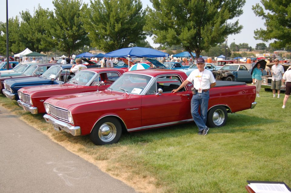 Red 1967 Ford Ranchero parked on grass with a man posing beside it