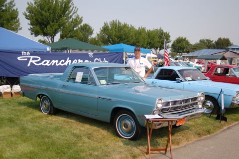 1967 Ford Ranchero - A light blue Ford Ranchero is displayed at an outdoor car show with a man standing beside it.