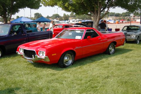 1967 Ford Ranchero - A red pickup truck with a bed is parked on the grass at an outdoor car show.