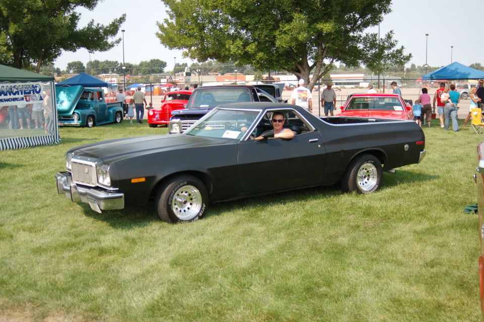 Flat black 1970s Ford Ranchero driven on grass at a car show, driver's side view
