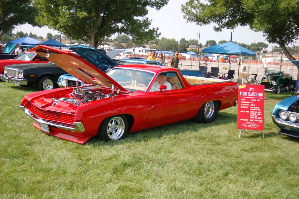 Red Ford Ranchero at car show, hood open on chromed engine, polished wheels