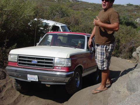 1994 Ford Bronco - A red and white 1994 Ford Bronco 4x4 is seen off-road with a man standing next to it, and another vehicle in the background.
