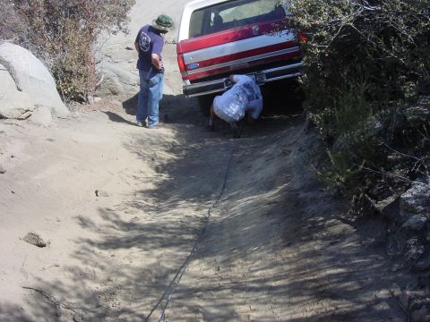1994 Ford Bronco - A red and white Ford Bronco is stuck on a steep dirt incline, with two individuals attempting to assist.