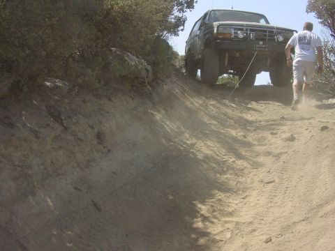 1994 Ford Bronco - A dark 1994 Ford Bronco is winched up a steep, dusty incline on a trail.