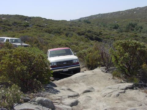 1994 Ford Bronco - Two SUVs navigate a rocky trail through a brushy, hilly landscape under a clear sky.