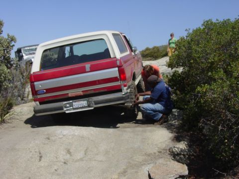 1994 Ford Bronco - Ford Bronco on a trail, with people checking the rear tire. Another vehicle is parked behind it.