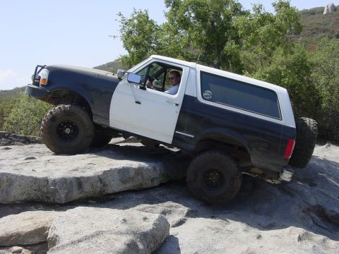 1994 Ford Bronco - A two-tone 1994 Ford Bronco navigates a rocky trail, demonstrating its off-road capabilities.