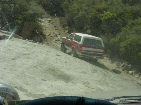 1994 Ford Bronco - Ford Bronco navigating a steep, rocky trail with dense foliage in the background.
