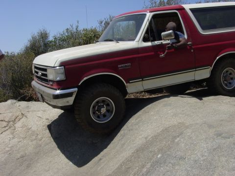 1994 Ford Bronco - A red and white Ford Bronco navigates a rocky terrain.