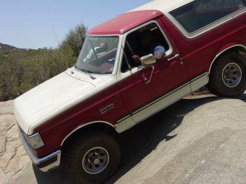 1994 Ford Bronco - A red and white 1994 Ford Bronco navigates a rocky terrain, its off-road capabilities.