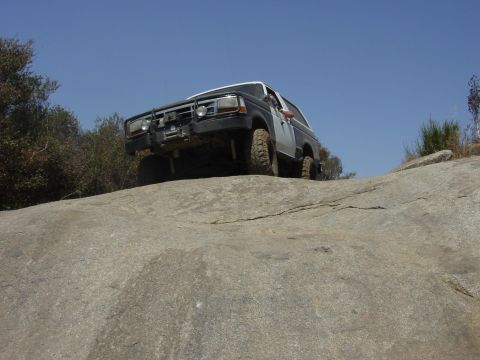 1994 Ford Bronco - A Ford Bronco navigates a rocky incline under a clear blue sky.