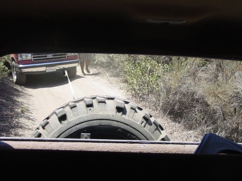 1994 Ford Bronco - Red Ford Bronco being towed on a dirt road, seen through the rear window of another vehicle.