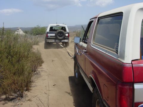 1994 Ford Bronco - Two Ford Broncos are seen on a dusty dirt road, one towing the other.