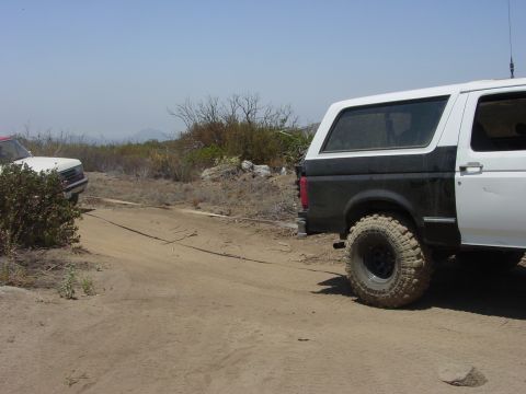 1994 Ford Bronco - Two SUVs are connected by a tow rope on a dusty, off-road path under a clear sky.