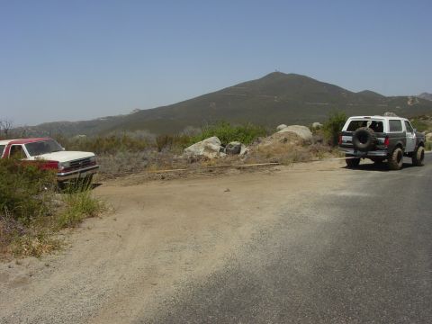 1994 Ford Bronco - Two SUVs are connected by a tow strap on a dirt road, with a mountain range visible in the distance under a clear sky.