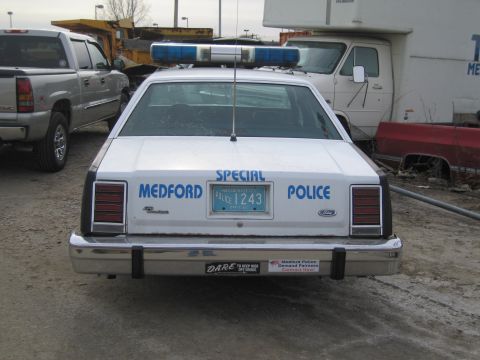 1991 Ford LTD Crown Victoria - Rear view of a white police car with 'MEDFORD SPECIAL POLICE' text and a blue light bar, parked outdoors.