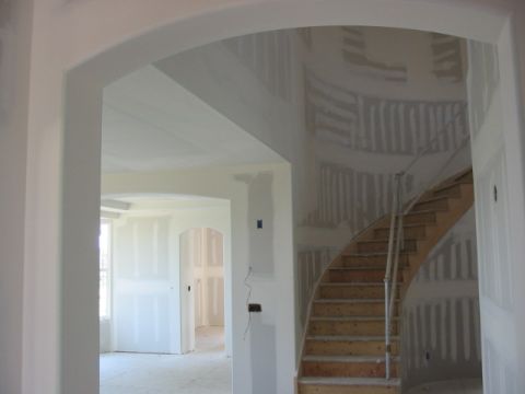 1995 Ford Bronco - A view through an archway reveals an unfinished interior with a curved staircase and walls covered in drywall.
