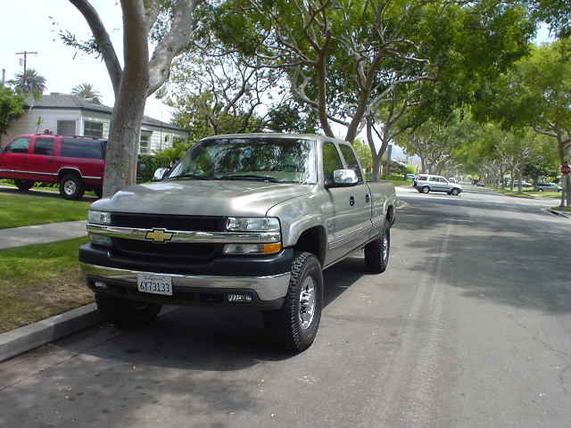 Silver 2002 Chevrolet Silverado 2500 parked on street, red SUV in driveway