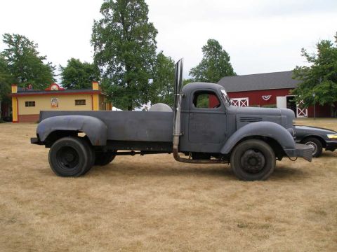 1997 Ford Taurus - Side profile of a vintage 1940s-era flatbed truck in flat gray primer with a tall polished vertical exhaust stack behind the cab, black ste…