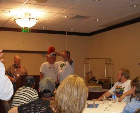1997 Ford Taurus - Indoor banquet-room award ceremony where one man places a novelty red-and-gold crown on another man's head while a third speaks at a podium…