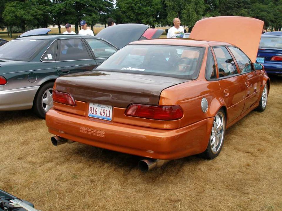 Rear view of custom orange Ford Taurus SHO sedan at a car show