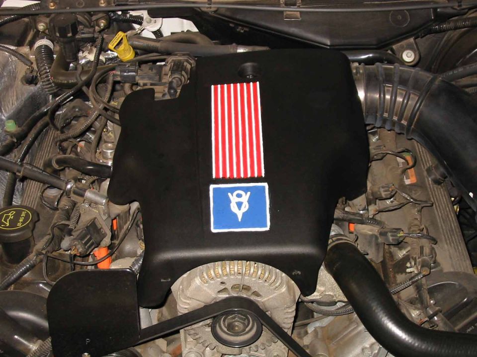 Engine bay with black engine cover featuring red stripes and a painted V8 logo