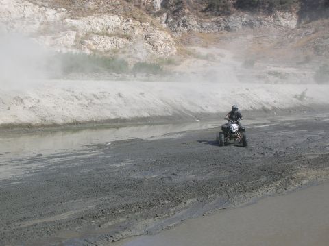 1985 Ford Bronco - An ATV rider navigates a dusty, muddy area next to a shallow waterway.