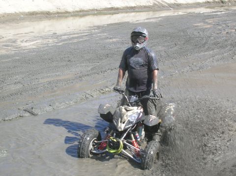 1985 Ford Bronco - A rider on an all-terrain vehicle navigates through a muddy terrain, kicking up spray.