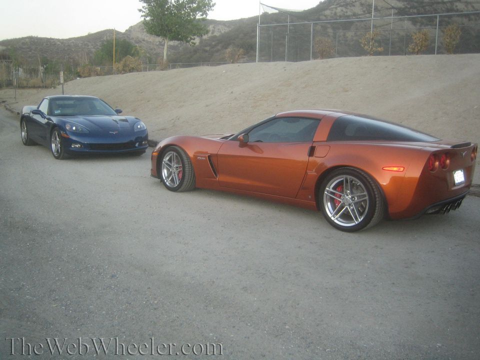Orange and blue Chevrolet Corvette coupes parked on gravel near a dirt hill