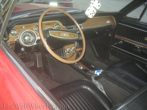 1990 Ford Bronco - interior of a red classic Mustang showing a woodgrain dash, round gauges, fuzzy dice and black bucket seats.