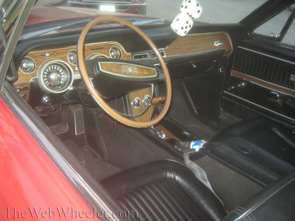 Interior of a classic Mustang with woodgrain dash, fuzzy dice and bench seats