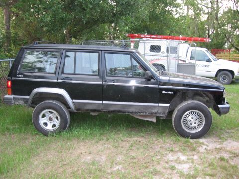 1974 Ford F-100 - A black Jeep Cherokee XJ is parked on a grassy area next to a white utility truck with ladders on top.