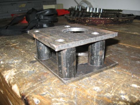 1974 Ford F-100 - A fabricated metal component rubber isolators is shown resting on a wooden surface, with tools in the background.