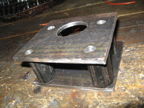 1974 Ford F-100 - A fabricated metal bracket with a circular opening and four bolt holes sits on a workbench.