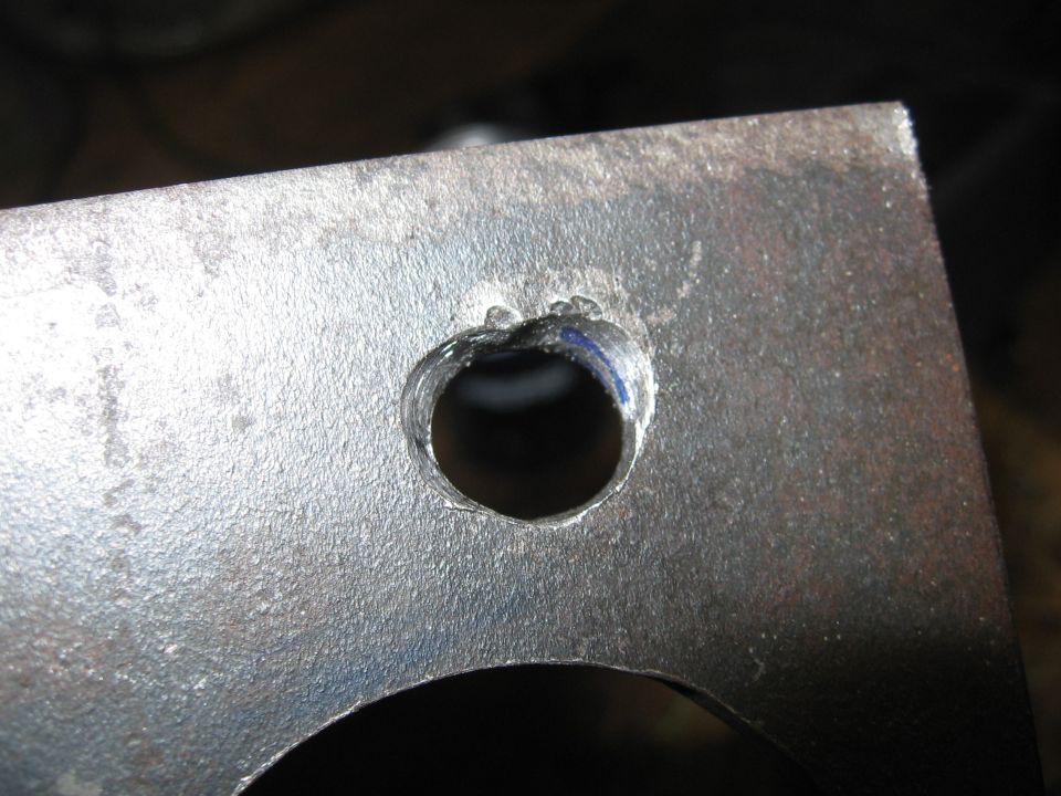 Close-up of a metal bracket with a drilled hole, showing rough edges and some blue marking
