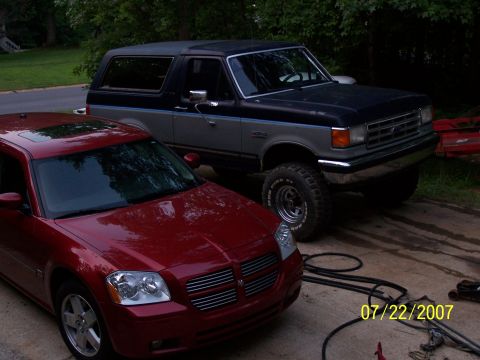 1979 Ford F-150 - A dark blue and gray Ford Bronco is parked on a driveway next to a red Dodge Magnum. The Bronco appears to be from the late 1980s.