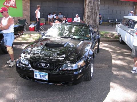 1989 Ford Mustang - A black Ford Mustang convertible is parked in front of a garage with people gathered around.