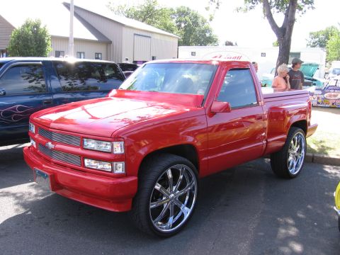 1989 Ford Mustang - A red pickup truck with custom chrome wheels is parked next to a blue SUV.