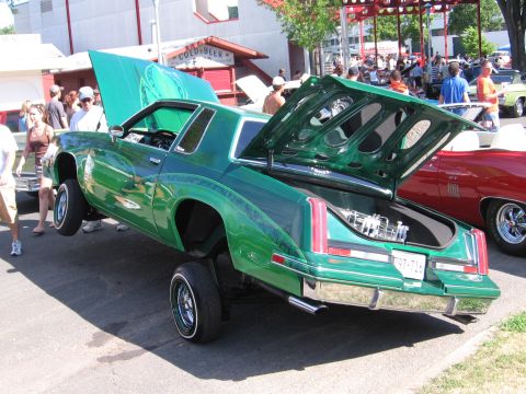 1989 Ford Mustang - A green lowrider with its hood and trunk open is displayed, with another car visible to the right.