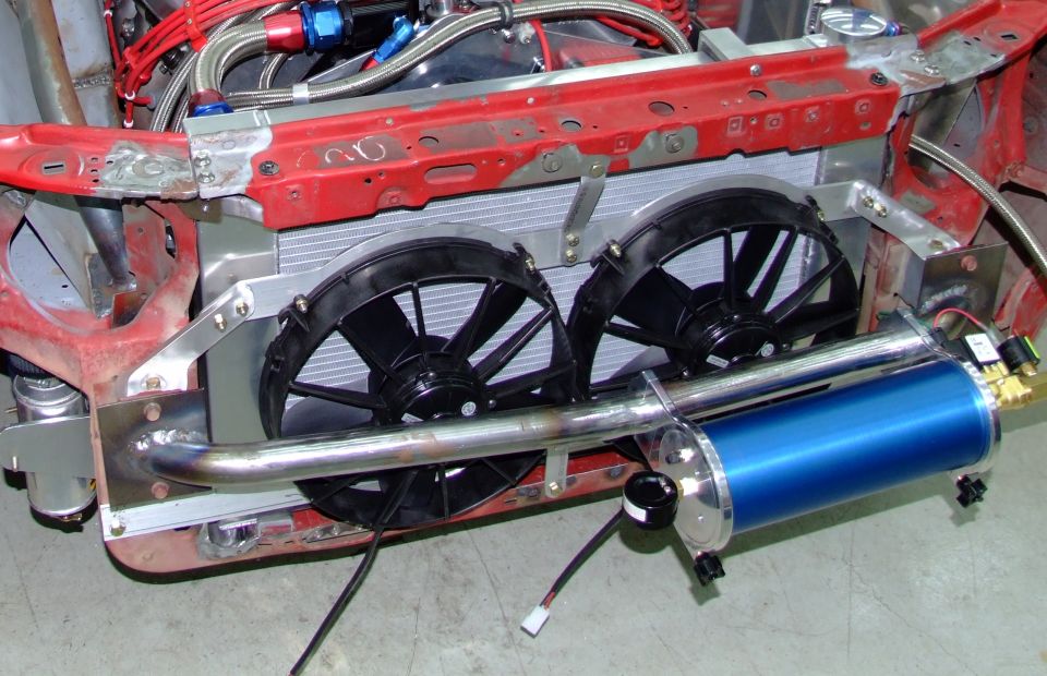 Engine bay with dual electric fans, radiator, and a blue canister. Some red metal framing is visible