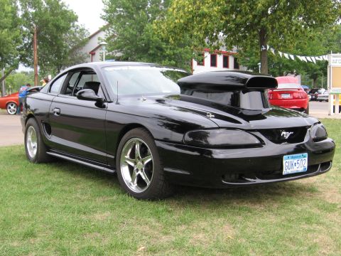 1989 Ford Mustang - A modified black Ford Mustang is parked on a grassy lawn with other vehicles in the background.